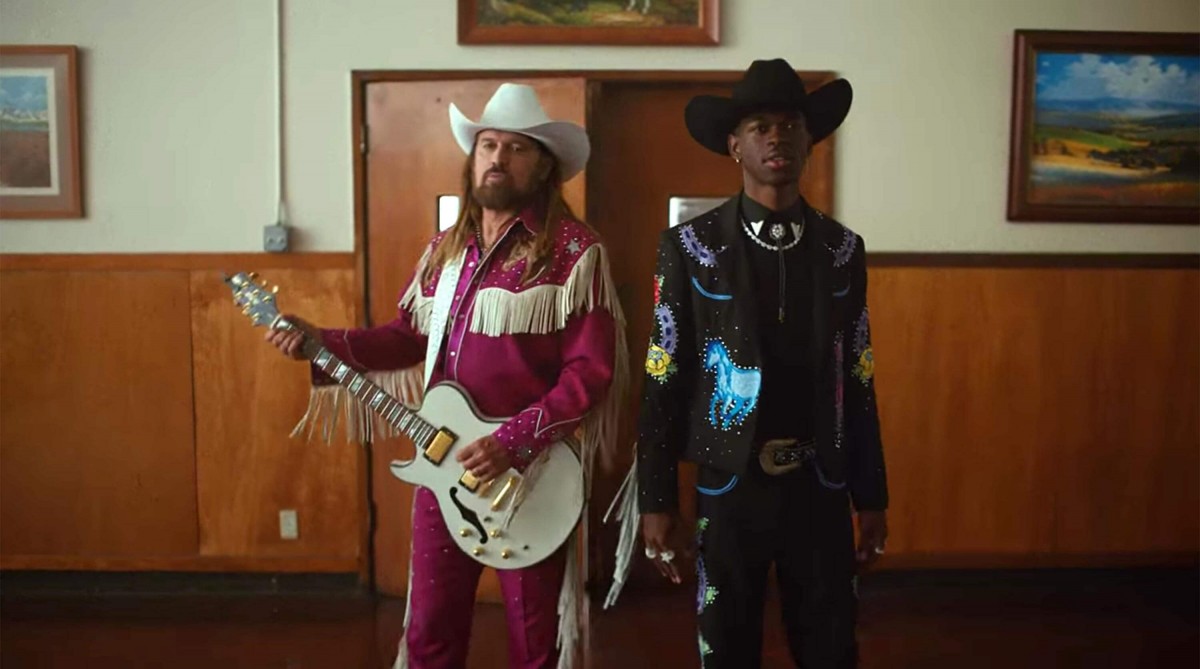 Lil Nas X mengenakan pakaian ala koboy berwarna gelap, berdiri bersebelahan dengan Billy Ray Cyrus, dalam salah satu adegan di video klip Old Town Road